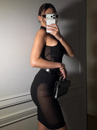 Person wearing a black outfit with sheer panels, holding a phone and a small handbag. #color_black
