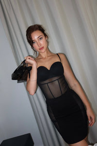 Woman wearing a black dress with sheer panels against a white curtain background #color_black