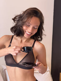Woman in a black bra holding a cup and saucer in a casual setting. #color_chocolate