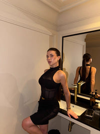 Woman in a black outfit standing in front of a mirror in a bathroom. #color_black