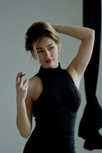 Woman in a black sleeveless dress posing against a plain background #color_black